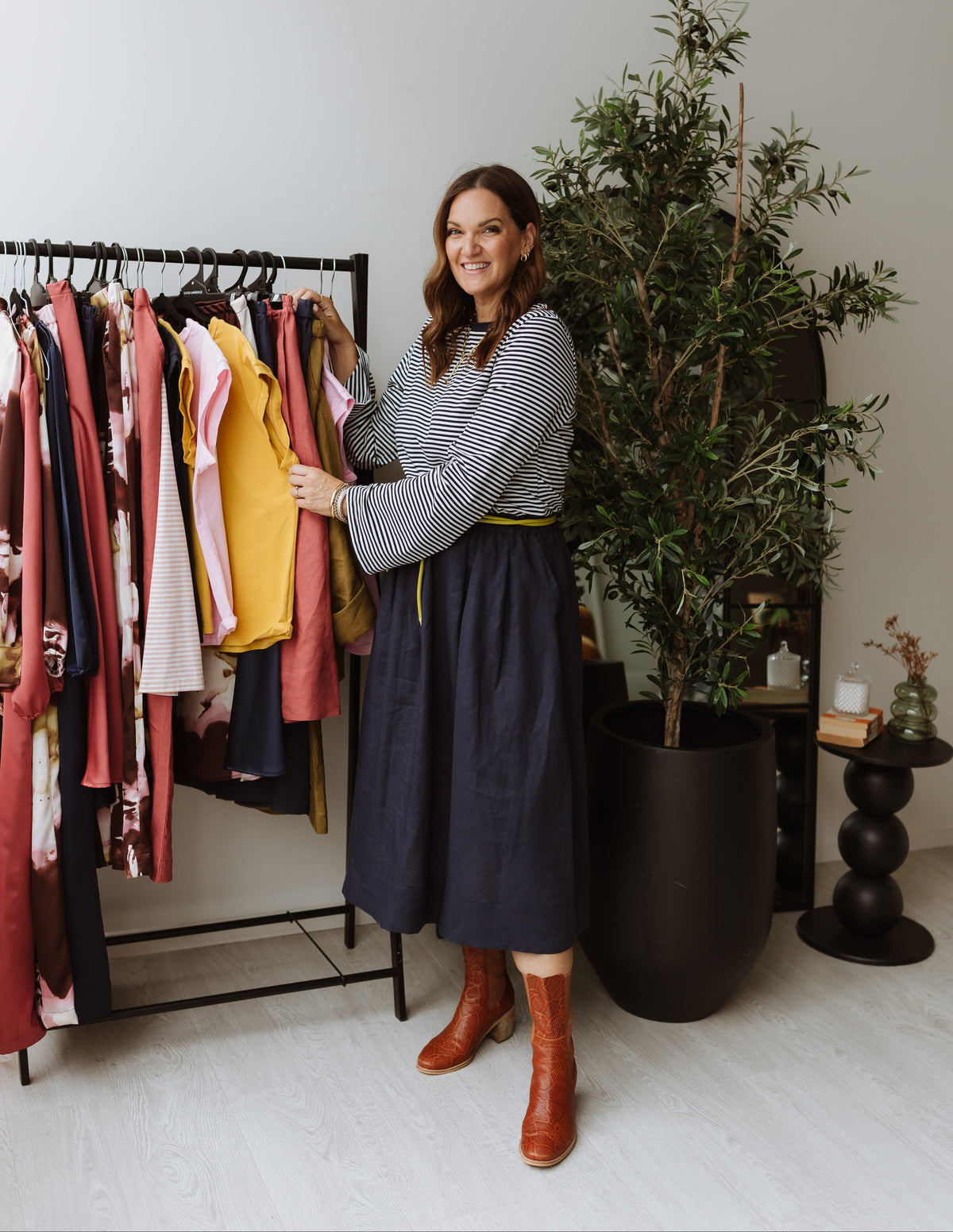 Woman standing next to a rack of clothes with a plant in the background